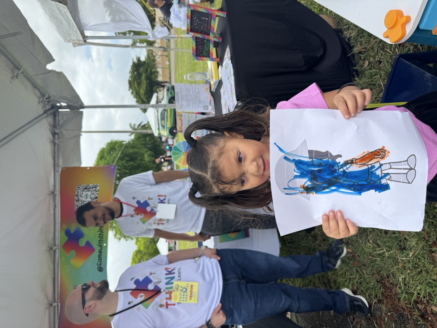 Blue skies and blue artwork — a child shows off their colorful creation with a g